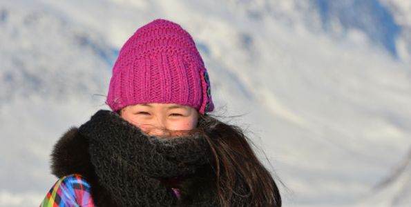 Photo d'une jeune personne portant un bonnet en tricot rose et un foulard marron foncé qui couvre la majeure partie de son visage. Elle se tient devant un arrière-plan enneigé.